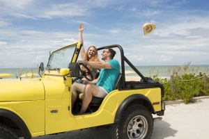 A couple drive along a Sanibel Island beach in their yellow Jeep