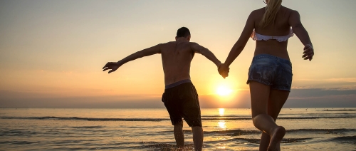 Couple running into water at sunrise