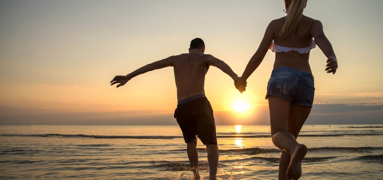 Couple running into water at sunrise